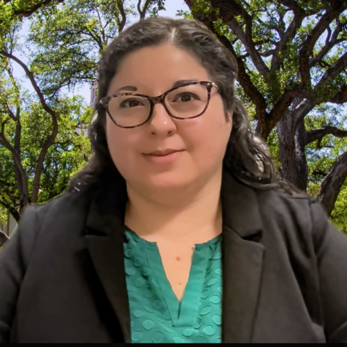 Latina female with long black hair wearing black glasses and a green shirt with a black jacket