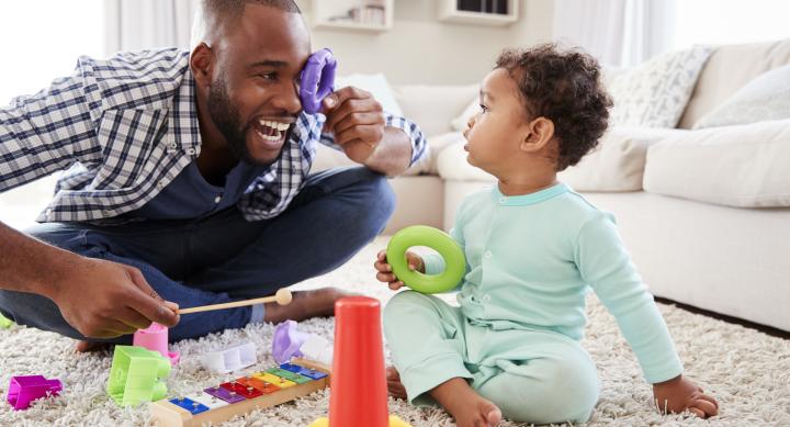 image of a dark skin short hair dad playing with his toddler who is wearing a mint color pajama